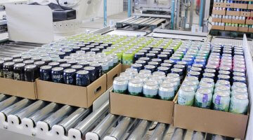 An automated conveyor system with mixed-case pallets carrying assorted canned beverages, illustrating the use of advanced palletizing technology for efficient distribution, reflecting diverse consumer preferences without compromising operational speed and efficiency.