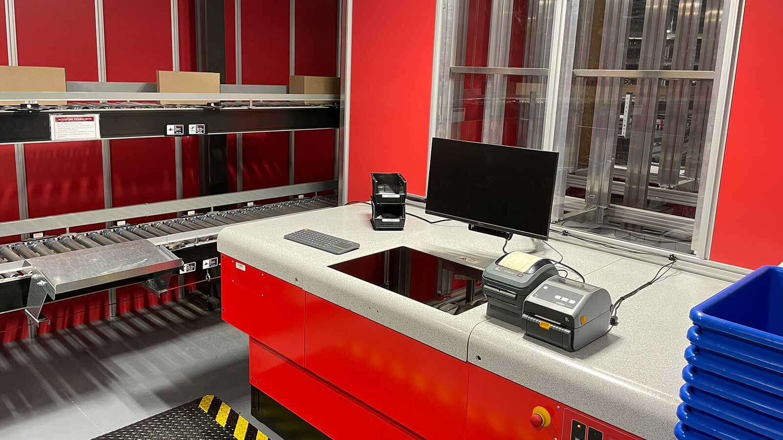 Outdoor Network AutoStore Pick Station for e-commerce order fulfillment. Two levels of case conveyor shown with a label printer.